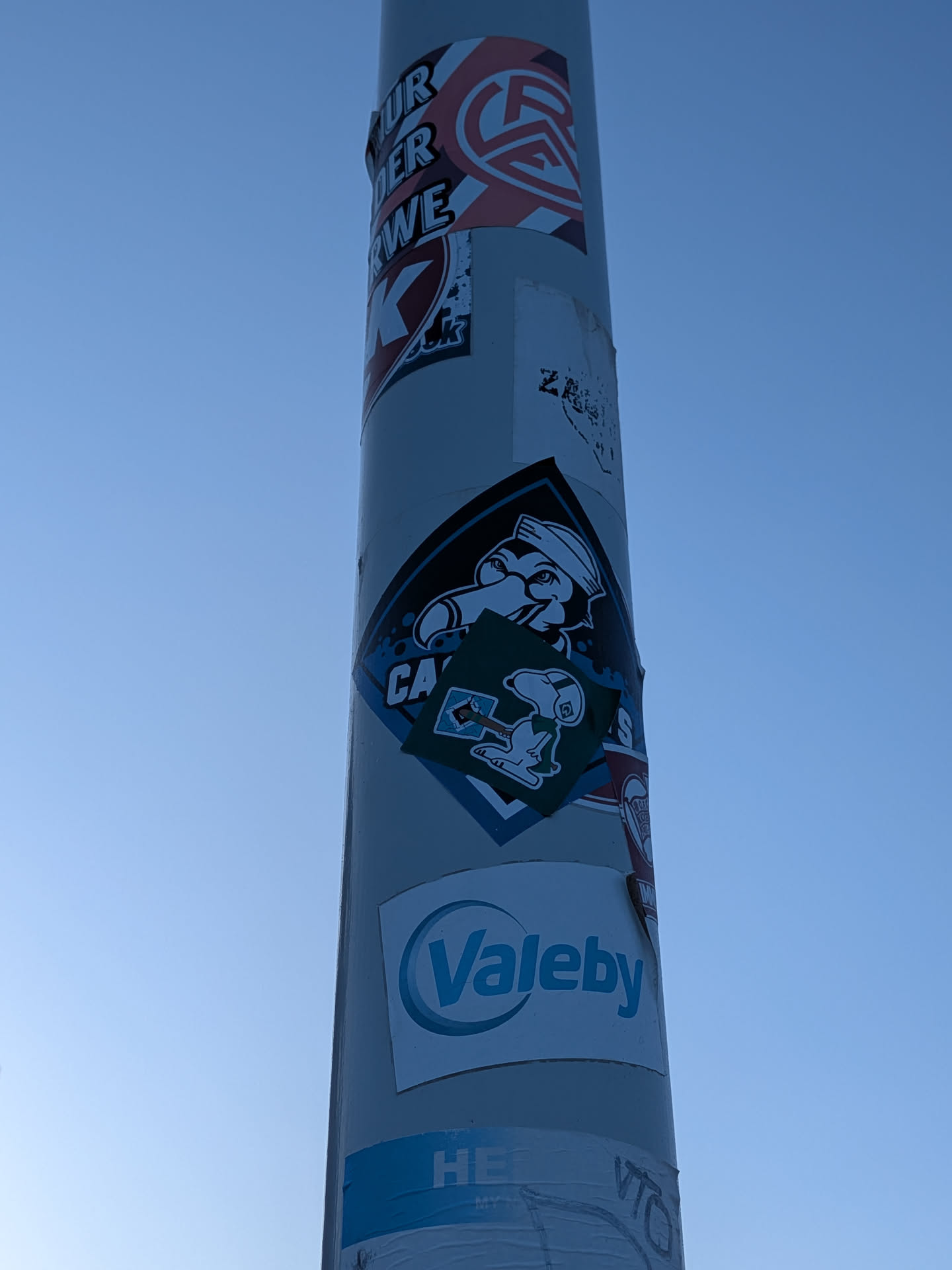A diamond-shaped sticker featuring a cartoon seagull wearing a sailor cap, with the text 'CASUALS' partially obscured. A smaller, square green sticker depicting Snoopy holding a flag is pasted directly over the center.