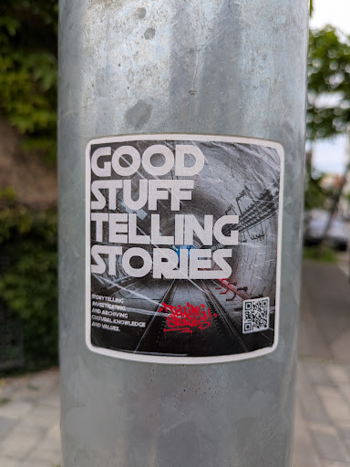 This sticker features the text "Good Stuff Telling Stories" in bold, white letters on a background that appears to be a railway or tunnel. The sticker also includes a small QR code on the right side and text at the bottom, which reads: "STORYTELLING INVESTIGATING AND ARCHIVING CULTURAL KNOWLEDGE AND VALUES."