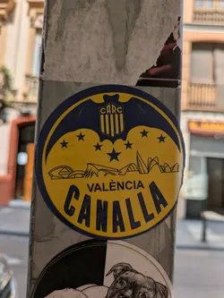 The sticker is oval-shaped with a blue border and yellow center. At the top, there's a shield with the letters 'CARC'. Below the shield, there are several stars and a depiction of architectural structures. The text 'Valencia' is above 'Canalla'.