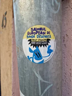 A sticker advertising the European Comics Festival, held in Bucharest from October 28th to November 21st, 2010.  The sticker features a cartoon character and the festival's details, including the location at MNAC, Galeria Etaj 3/4, Teatrul National Bucuresti. A website address is also visible.