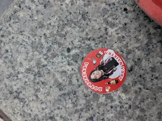 Street sticker Circular red sticker showing a woman in a doctor's coat with a stethoscope and cigarette. Surrounding icons include a pigeon, beer, and cigarettes. White text reads 'DOTTORESSA ARGA MAISTRA'.
