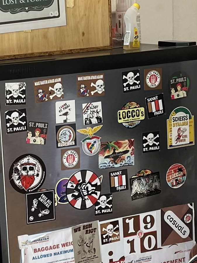 A circular sticker featuring a dynamic design of alternating red and white wedges, resembling a pinwheel or a target. At its core, a bold black clenched fist is raised upwards, symbolizing resistance and solidarity. The fist has some faint white text on it, which is too blurry to decipher accurately. The overall aesthetic is strong and impactful, reflecting a rebellious or activist theme.