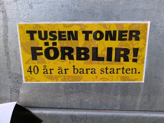 Street sticker Yellow sticker with black text.  The text says "Tusen Töner Förlir!" which translates from Swedish to "A Thousand Tones Remain!"  Below it, in smaller text, it says "40 år är bara starten." which translates to "40 years is just the beginning."