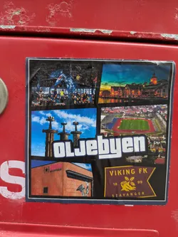 Street sticker The sticker is a multi-panel collage showcasing various aspects of Stavanger. It includes an image of football fans, likely supporters of Viking FK, followed by a scenic view of Stavanger's waterfront at dusk. Another panel features the 'Sverd i fjell' (Swords in Rock) monument, a historical landmark, and an aerial shot of a football stadium, presumably SR-Bank Arena. The collage also depicts the Lervig Aktiebryggeri building. Prominently displayed is the crest of Viking FK, the local football club, with its establishment year '1899' and 'STAVANGER'. The large, stylized text 'OLJEBYEN' (Oil City) overlays the central images, referring to Stavanger's key industry.