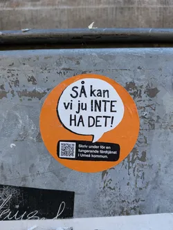 The sticker is circular with an orange border and a white speech bubble in the center. The speech bubble contains bold black text that reads 'SÅ kan vi ju INTE HA DET!'. Below the speech bubble, on a black rectangular background, is a QR code and text in Swedish. The text reads 'Skriv under för en fungerande färdtjänst i Umeå kommun.' The overall design is simple and direct, conveying a message of dissatisfaction and a call to action.