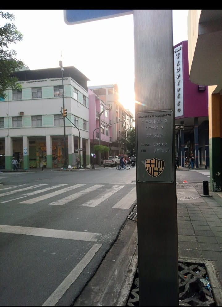 A rectangular, metallic grey plaque affixed to a pole. The top section displays the street name 'AGUIRRE Y SEIS DE MARZO' in capital letters, followed by corresponding braille text. Below this, the word 'RUTAS' (Routes) is visible, also accompanied by braille, and the number '638'. At the bottom of the plaque, a shield-shaped emblem is present, which is the crest of FC Barcelona. The crest features the St. George's Cross, the red and yellow stripes of the Senyera, and the club's initials 'FCB' over blue and red vertical stripes, with a football in the center.