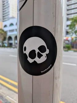 Street sticker A circular black sticker featuring a stylized white skull graphic in the center. The text 'NeverEnough.cz' is printed in small white font along the bottom right edge.