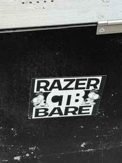 Street sticker A rectangular sticker with a black background and white design elements, stuck onto a textured black surface. The sticker displays bold white text in three rows: 'RAZER' at the top, 'CTB' in the middle, and 'BARE' at the bottom. On either side of the central 'CTB' text are mirrored illustrations of an angry, muscular cartoon dog resembling Snoopy, shown with clenched fists and a fierce expression.