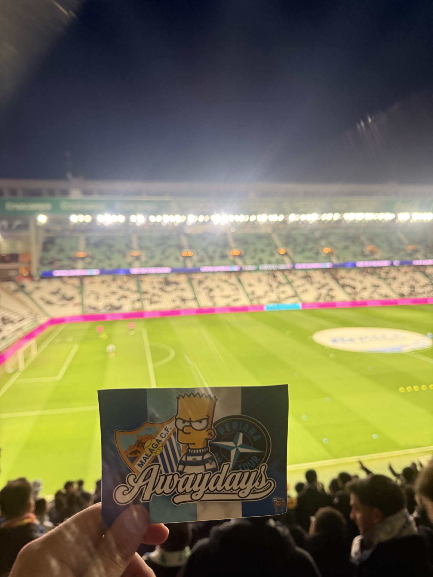 A rectangular sticker featuring Bart Simpson in a blue and white striped shirt, looking somewhat grumpy. The background is split, with light blue and white vertical stripes on the left and a solid dark blue on the right. To Bart's left is the crest of Malaga C.F., predominantly light blue and orange. To his right is a circular logo with a compass rose design and the text 'PERIANA TOUR' in white on a dark blue background. The word 'Awaydays' is prominently displayed across the bottom in a stylized, script font with a white outline and black shadow.