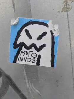 Street sticker A blue and white square sticker features a ghost-like character with angry black eyes and a jagged mouth. The style is reminiscent of graffiti art with thick black outlines. Text below the character reads 'MUFO INVDS'. The sticker is adhered to a gray surface.