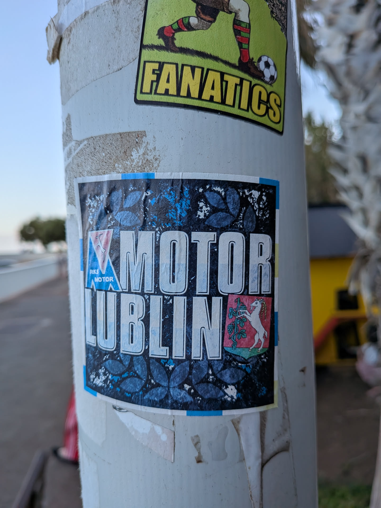 A square sticker featuring 'MOTOR LUBLIN' in bold white text. It displays the RKS Motor club logo on the left and the Lublin coat of arms on the right, over a dark leaf-patterned background with blue and yellow side borders.