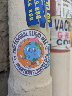 Street sticker This vibrant sticker showcases a cartoon depiction of Earth, complete with a pink bow, blushing cheeks, and expressive eyes. The Earth figure is playfully walking with cartoon shoes. The sticker is encircled with the text 'PROFESSIONAL FLIGHT RISK' at the top and 'IRISHTRAVELADDICT.COM' at the bottom. The design is completed with social media icons for TikTok and a username @IrishTravelAddict