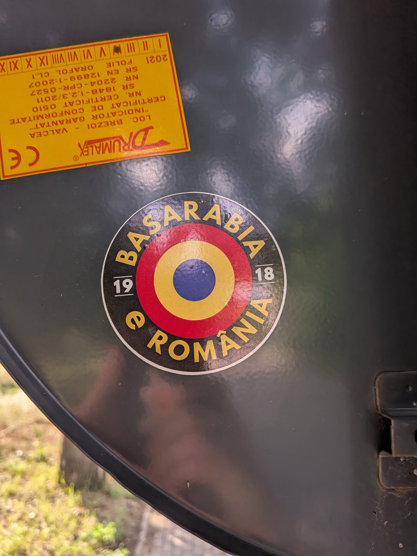 A circular sticker featuring concentric circles in the Romanian national colors (blue, yellow, red) surrounded by a black outer ring. The ring contains the yellow text 'BASARABIA' and 'e ROMÂNIA', split by the white numbers '19' and '18'.