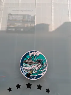 The sticker is circular with a white border. The main design depicts a grey military-style helicopter flying over large, stylized teal and white ocean waves. Below the helicopter, a dark grey object resembling a bomb or torpedo with a yellow band is shown descending into the waves. The word 'RIPTIDE' is written vertically along the left edge of the circle, and the year '2024' is displayed at the bottom right. The overall design evokes a theme of naval or military operations, possibly an exercise or event.