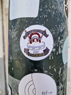 Round sticker with a logo. The logo contains a drum with a magnet above it and two crossed hammers behind the magnet. The text ISEC COIMBRA is visible at the bottom of the sticker. The text on the top seems to say 'ISECOTUNA'.