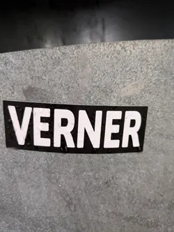 Street sticker A black and white sticker with the name VERNER written in capital letters. The sticker is affixed to a gray metallic surface.