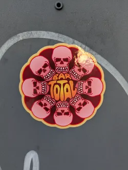 Street sticker Round sticker with a dark red background and a beige border. Eight pink skulls with grinning teeth surround the text "BAR TOTAL" in an orange gradient. The design has a 70s vibe.