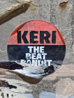Street sticker Round sticker with the text "KERI" on top in large, bold, black letters on a pinkish-red background, and "THE BEAT BANDIT" below in smaller, white, bold letters on a black background.  A website address is visible at the bottom. 