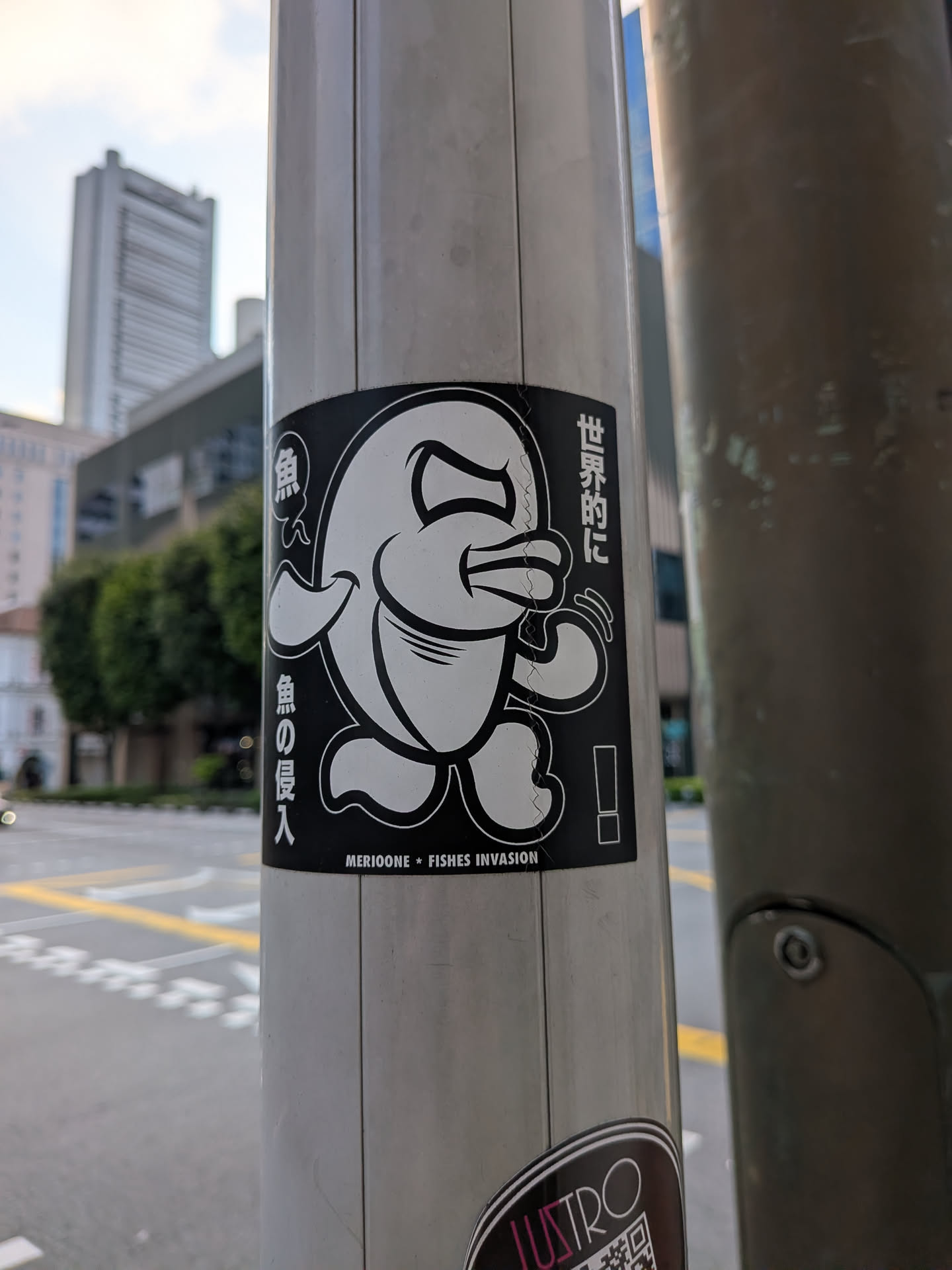A rectangular black sticker depicting a stylized, walking cartoon fish character with an expressive face. The design uses bold white outlines on a black background, accompanied by vertical Japanese text on the sides and English text at the bottom.
