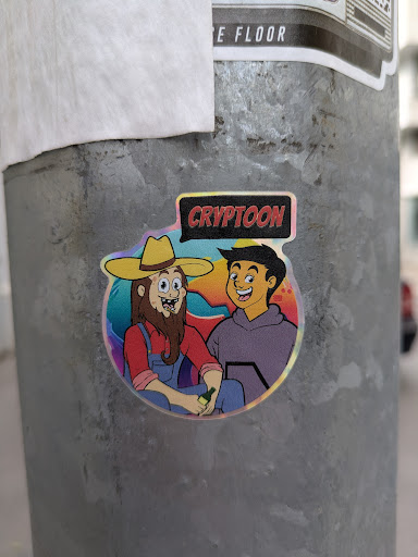 This sticker shows two cartoon characters. The left character has a long beard, overalls, and a cowboy hat. He is holding a bottle. The right character wears a hoodie. Above them reads "CRYPTOON". The sticker has a colorful, rainbow effect background.