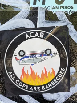 Street sticker The sticker shows a black and white circular design. The text "ACAB" is at the top, and "ALL COPS ARE BARBECUES" is at the bottom. In the center, there is a cartoon of an upside down police car above flames.