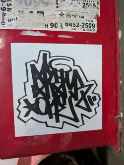 Street sticker Square white sticker featuring a bold black graffiti handstyle tag with a thick outline, pasted on a red metal surface.