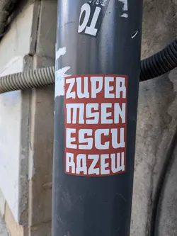 A red rectangular sticker with stylized white block lettering on a dark grey pipe.