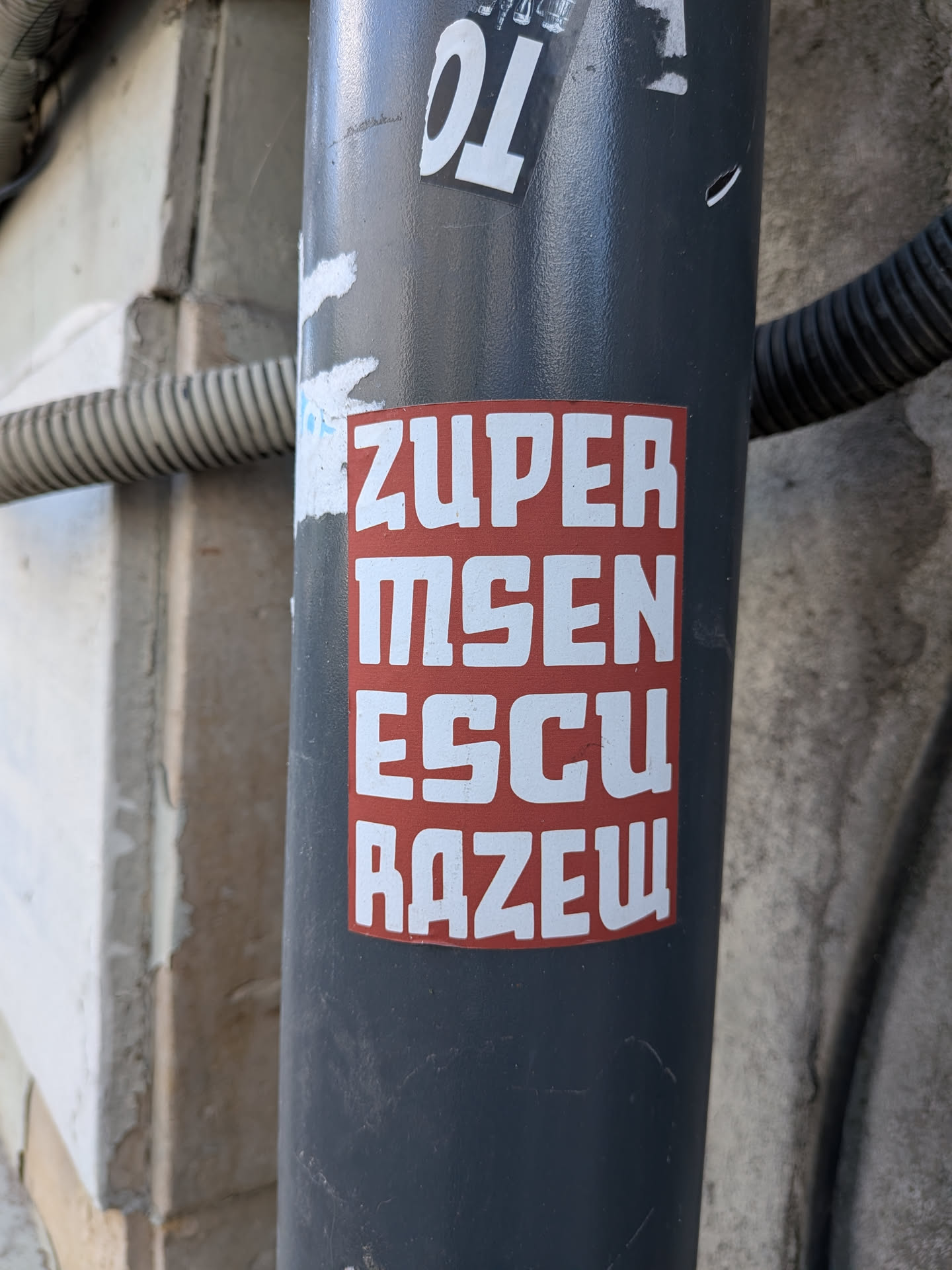 A red rectangular sticker with stylized white block lettering on a dark grey pipe.