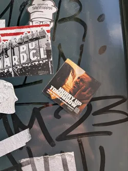 Street sticker A square, tilted sticker depicting a warm-toned, intimate close-up of a couple. It features the bold white title 'HURRY UP TOMORROW' and Romanian promotional text 'DIN 16 MAI DOAR IN CINEMATOGRAFE' at the bottom, alongside studio logos and a small QR code.