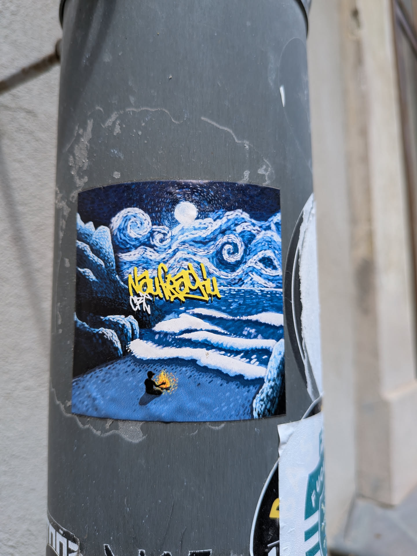 Rectangular sticker showing a post-impressionist night beach. A figure sits by a campfire under a swirling sky and moon. A yellow graffiti tag 'Naufrago' is in the center.