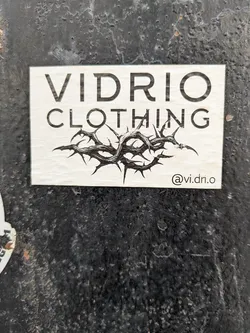 A rectangular sticker advertising "Vidrio Clothing". The sticker features the company name in bold letters above an image of a crown of thorns. The Instagram handle @vi.dri.o is printed below the image.