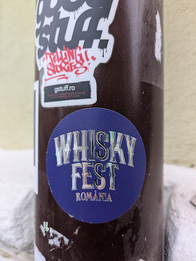 A circular sticker with a blue background. The text "WHISKY FEST" is displayed in a holographic, stylized font. Below that, "ROMANIA" is written in smaller, similar font.