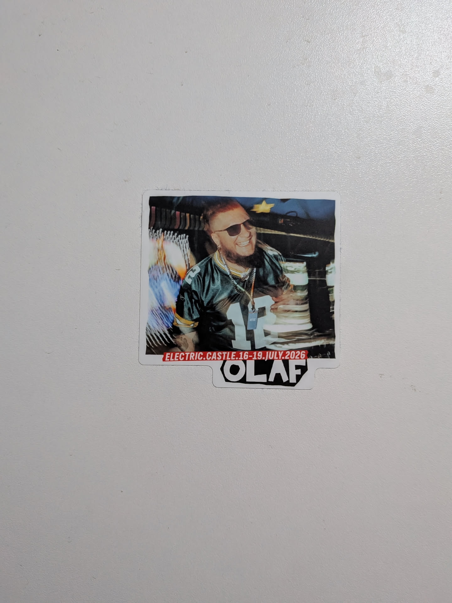 Die-cut sticker featuring a photo of a bearded man in sunglasses and a Green Bay Packers jersey. A red banner at the bottom reads 'ELECTRIC.CASTLE.16-19.JULY.2026', with 'OLAF' printed in bold black text below.