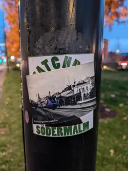 Street sticker A sticker featuring an illustration of the Södermalm train station in Stockholm. The style is reminiscent of vintage travel posters.  The sticker also has partially visible text that seems to read "ATCHA" above the illustration. At the bottom, it clearly says "SÖDERMALM".
