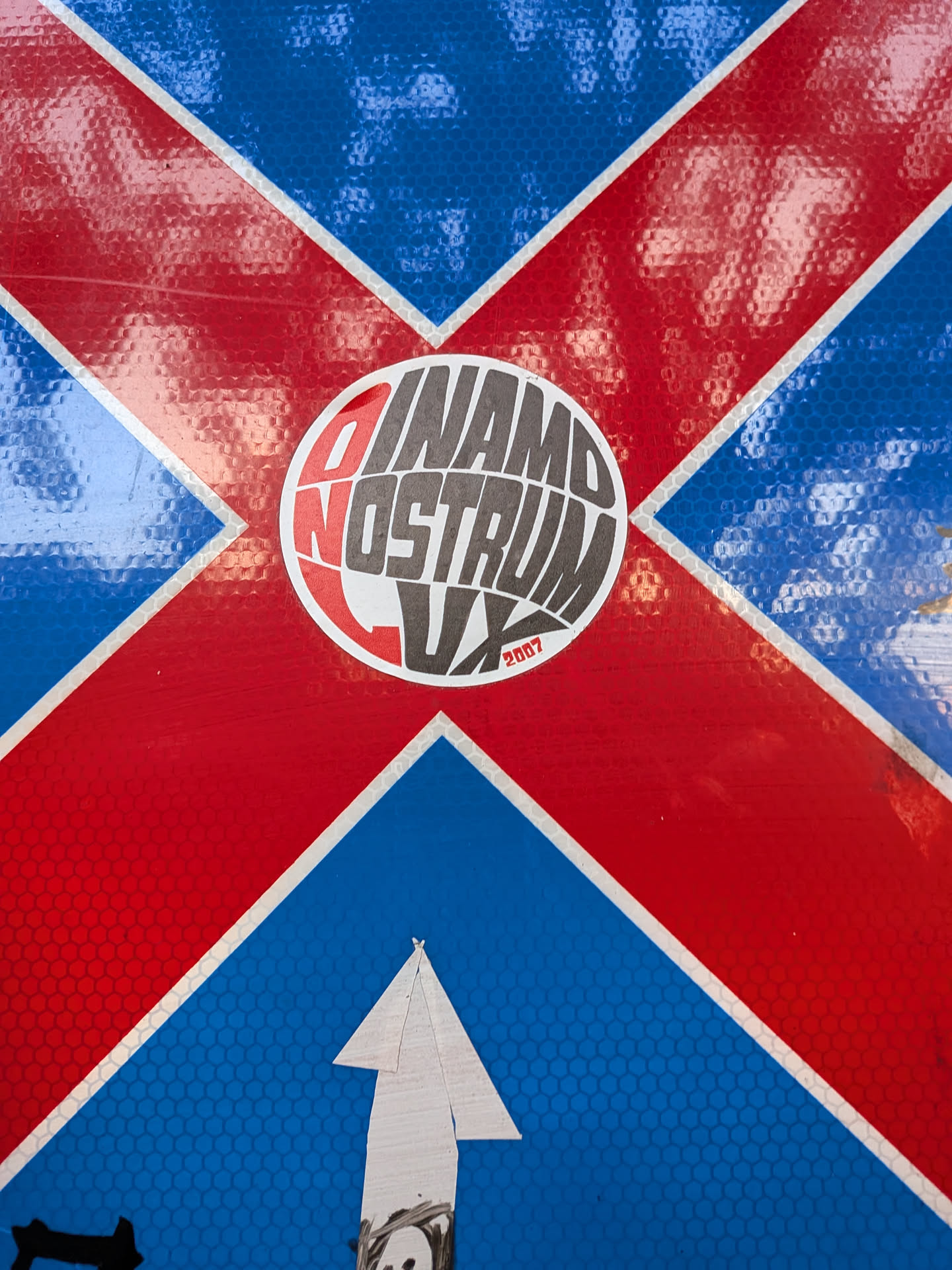 A round sticker featuring warped, stylized text in dark grey and red on a white background, reading 'DINAMO NOSTRUM LUX' with '2007' in small red font at the bottom right.