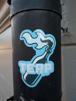 Street sticker The sticker features a stylized representation of a Molotov cocktail. The bottle is depicted in dark teal with a white label and a white wick. Emerging from the bottle's opening is a plume of light blue and white smoke or flame, outlined in dark teal. Below the bottle, the word 'TERP' is prominently displayed in large, blocky, light blue letters with a white outline and a subtle pixelated effect. The entire design is bordered by a thick, light blue outline.
