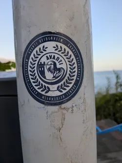 A circular, weathered blue and white sticker on a pole. It features a central emblem of a knight's helmet and castle tower, surrounded by a laurel wreath. The outer border repeats the text 'AVANTI HEIDENHEIM'.