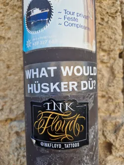 Street sticker A black and gold sticker with the text "Ink Floyd" in a stylized script font. Below the main text is the Instagram handle @inkfloyd_tattoos.  Above the sticker is another sticker with the text "What would Hü̈sker Dü̈?"