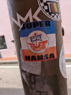 Street sticker Rectangular sticker with blue, white, and red horizontal stripes. Features the F.C. Hansa Rostock crest in the center, with 'SUPER' written on the top blue stripe and 'HANSA' on the bottom red stripe.