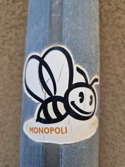 A sticker featuring a cartoon bee with the word MONOPOLI visible at the bottom. The sticker is slightly worn and has some cracks.