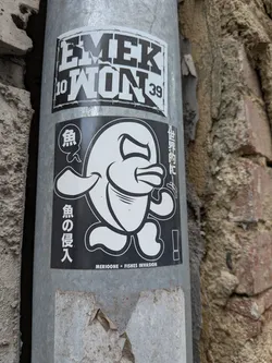 Street sticker A rectangular black and white sticker depicting a stylized, angry cartoon fish with legs. It features Japanese text on the sides and 'MERIOONE * FISHES INVASION' printed along the bottom edge.