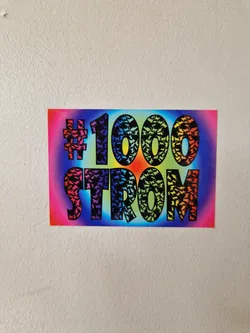 Street sticker A rainbow-colored sticker with the text '#1000Strong'. The numbers and letters are filled with small, repeated black icons that resemble bats or birds.  The background is a gradient of colors including pink, orange, yellow, green, blue, and purple.