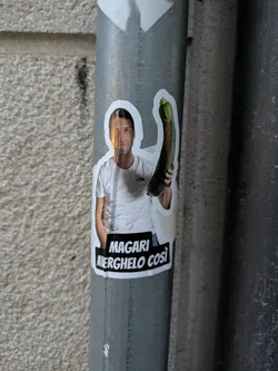 Street sticker The sticker shows a man wearing a white t-shirt and holding a long, green zucchini. Below the man, there is text on a black rectangle.