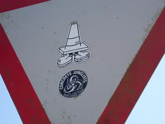 Street sticker Two stickers placed vertically. The top sticker is a white die-cut cartoon traffic cone character with legs and sneakers, featuring 'DRONEBOY' on one shoe. The bottom sticker is a black circular decal with a coiled snake logo, reading 'CONCRETE JUNGLISTS' and 'WORLDWIDE TRIBE'.