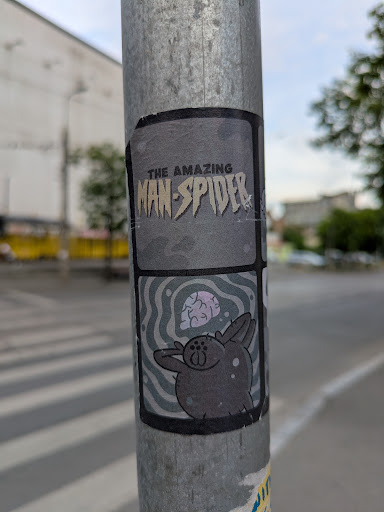 A sticker on a metal pole with a cartoon spider with a brain floating above. The sticker references Spider-Man with the words 'The Amazing Man-Spider'.