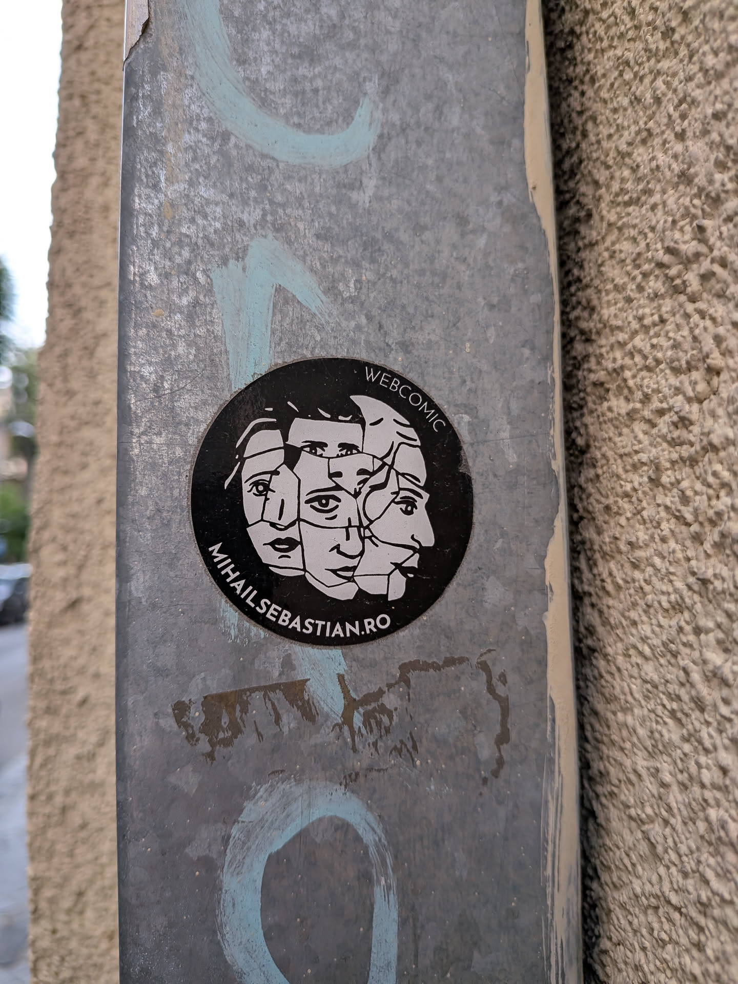 A circular black sticker featuring a white graphic of shattered, overlapping faces. Text along the border reads 'WEBCOMIC' and 'MIHAILSEBASTIAN.RO'.