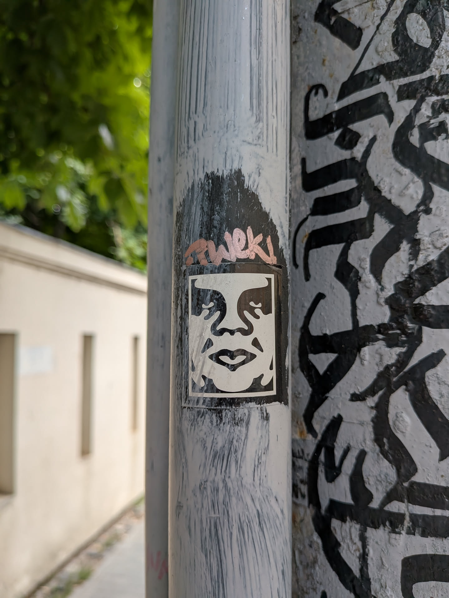 A rectangular black and white sticker depicting the stylized, high-contrast face of Andre the Giant. It is pasted on a grey metal pipe with hand-written graffiti above it.