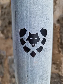 Street sticker Close-up of a black vinyl sticker featuring a stylized wolf's head encircled by leaf-like shapes, adhered to a weathered gray metal pole. The sticker has a minimalist design with a strong graphic presence.