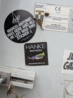 Street sticker A square black sticker featuring the text 'HANKE BROTHERS' in white. Below the text is a colorful, stylized illustration of a hybrid musical instrument combining a violin, trumpet, and piano keys. The website 'www.hankebrothers.de' is printed at the bottom.