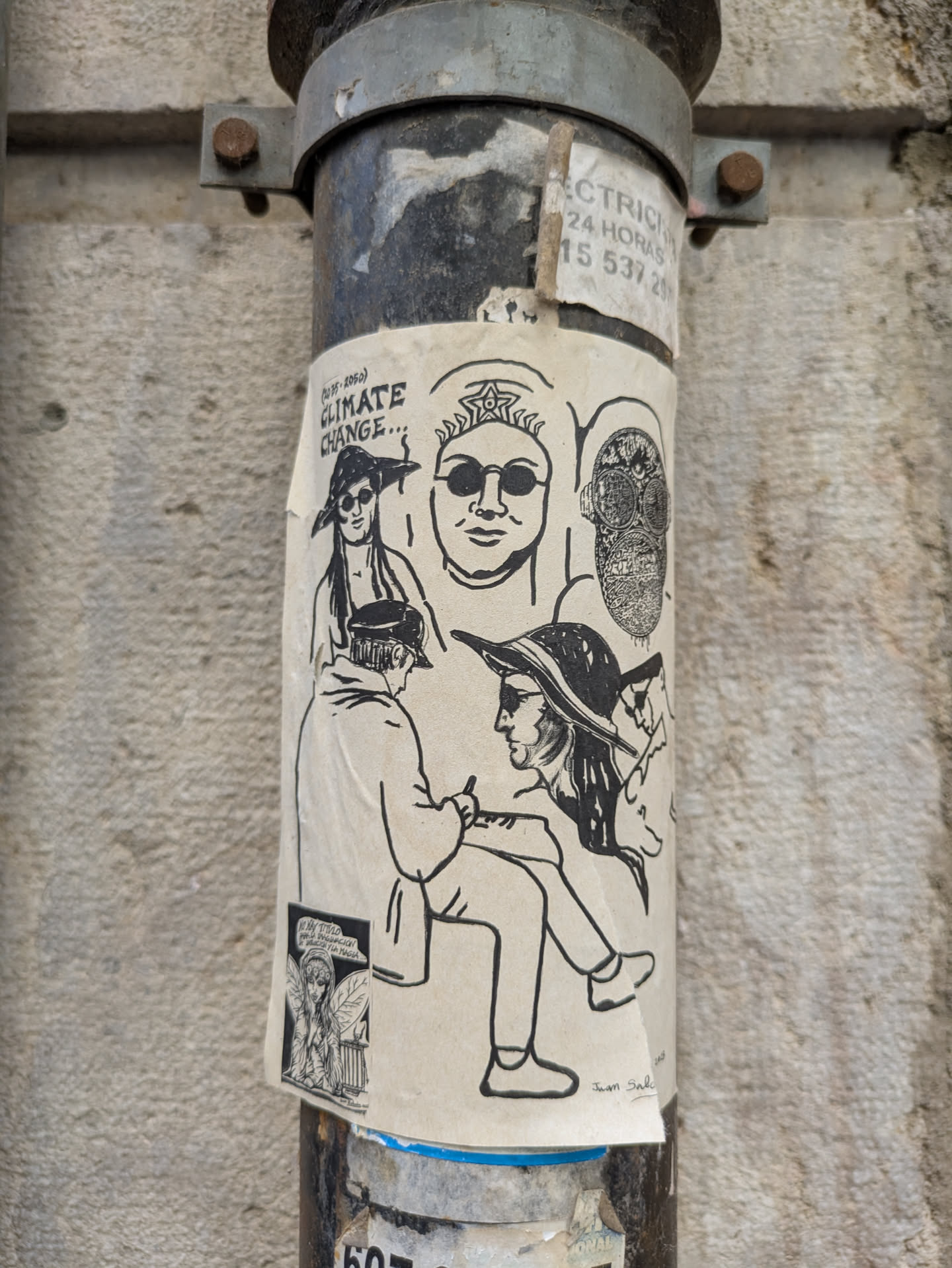 The sticker features a collage of black and white drawings on a neutral background. The drawings include people wearing hats and glasses, and a steampunk-esque mask. The text reads 'Climate Change...' and includes the signature 'Juan Salc'. There's another smaller sticker on the lower left, depicting a fairy-like character. The sticker is affixed to a gray, industrial metal pipe.